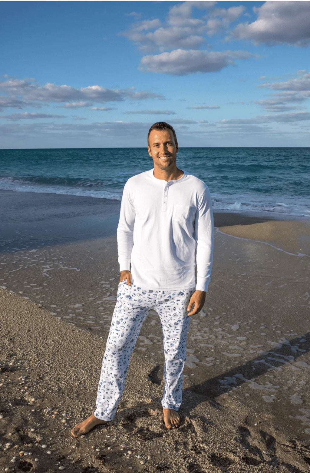 Embracing both comfort and coastal allure, a man stands confidently on the beach, dressed in stylish Erica Wilson pajamas